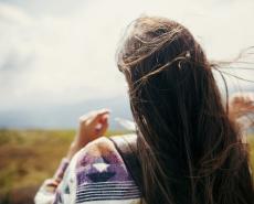 Donna con capelli al vento su un prato, sensazione di libertà e serenità.