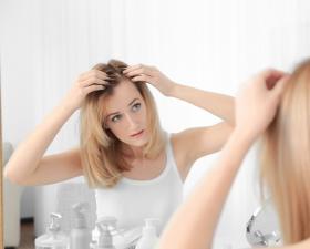 Donna guarda i capelli allo specchio, preoccupata.