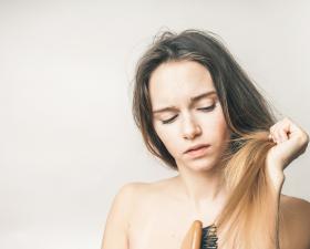 Donna pettina i capelli con espressione preoccupata.