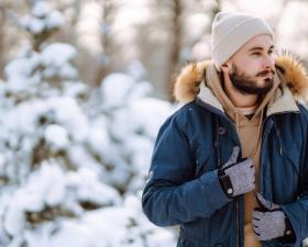 Uomo con giacca invernale e guanti, in un paesaggio innevato.