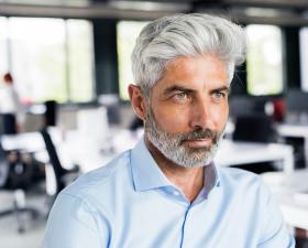 Uomo con capelli grigi in ufficio, sguardo serio.