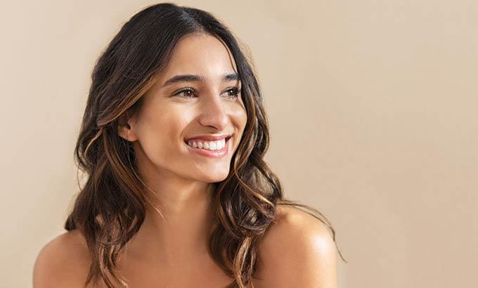 Donna sorridente con capelli castani ondulati su sfondo neutro.